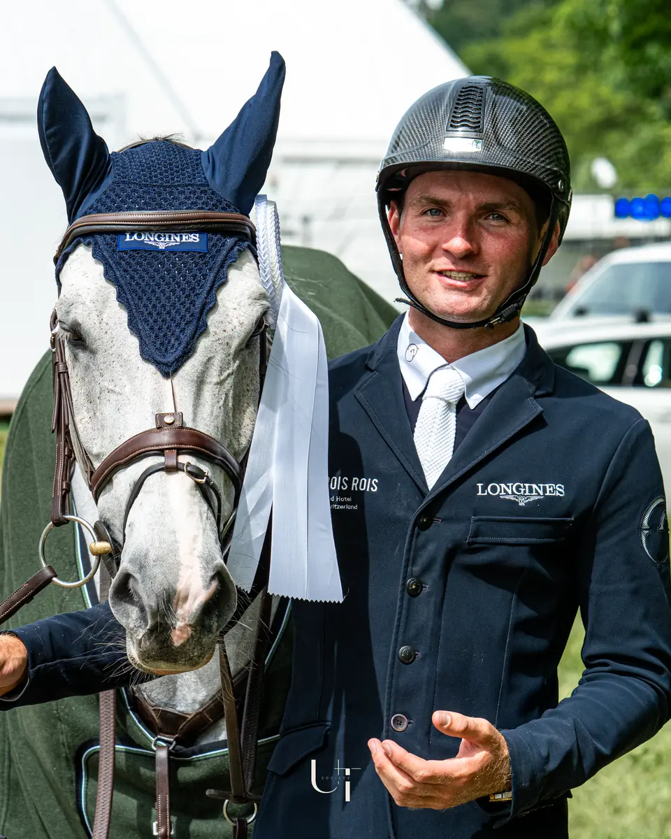 Bryan Balsiger beside his grey show jumper, the winner's rug over its shoulders